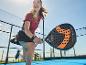 Frau spielt Padel mit schwarzem und orangefarbenem Padelschläger auf blauem Platz.