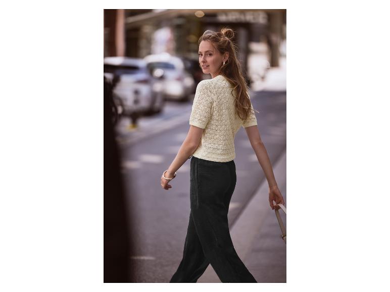 Frau geht auf der Straße, trägt einen hellgelben Pullover und schwarze Hosen.