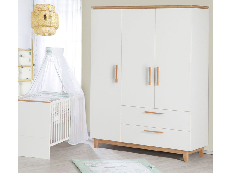 Ein weißes Babybett mit Himmel und ein weißer Kleiderschrank mit Holzteilen.