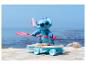 Stitch-Figur auf Skateboard mit Paddel, am Strand.