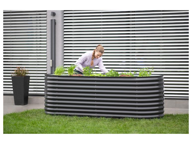 Frau pflegt Kräuter und Gemüse in einem großen Hochbeet auf einer Terrasse.