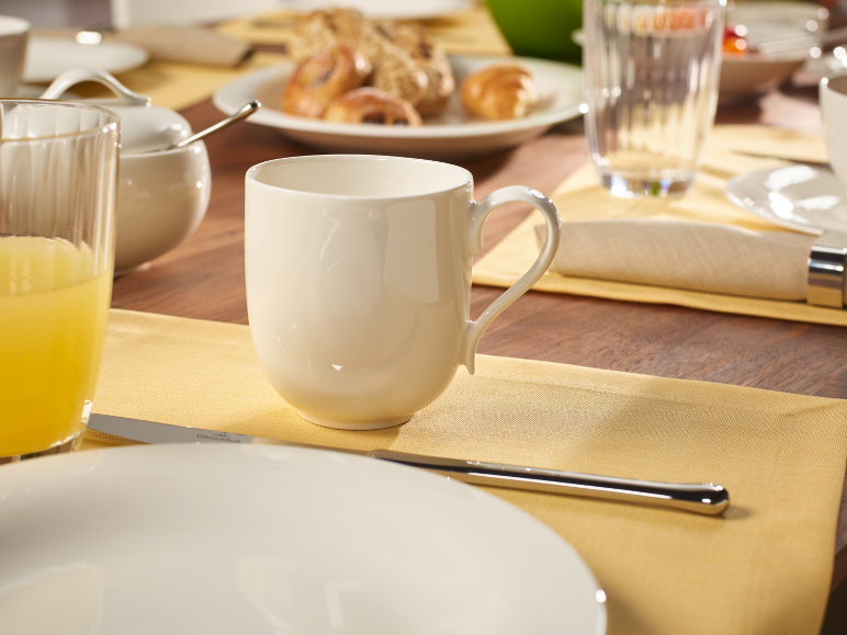 Frühstückstisch mit einer weißen Tasse, Orangensaft und Gebäck auf einem Holztisch.