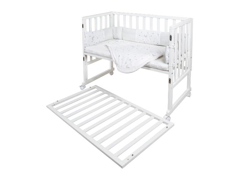 Weißes Babybett mit Mond- und Sternenmuster-Bettwäsche, mit abnehmbarem Matratzenrost.