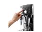 Hand drückt Knopf einer Espressomaschine, Glas wartet darunter.