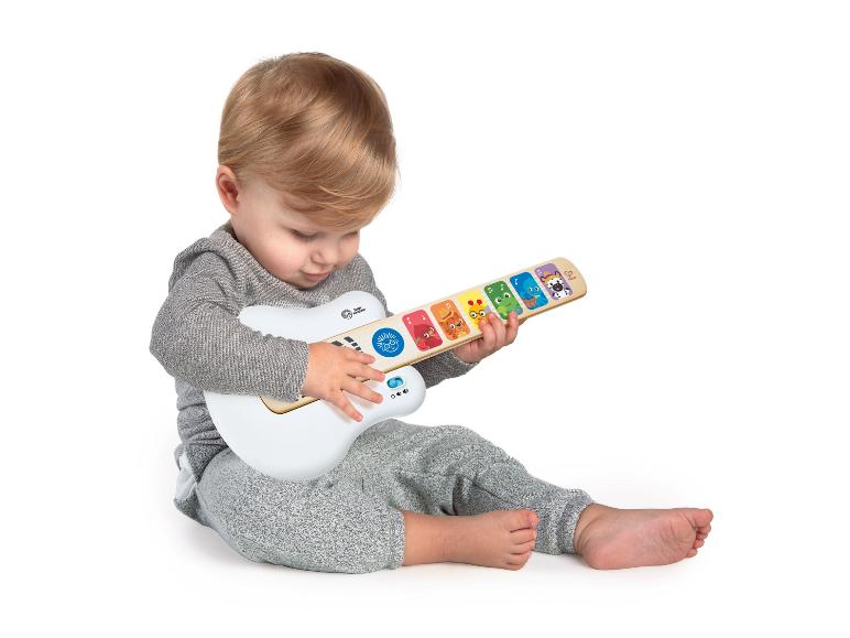 Kleinkind spielt mit einer weißen und hölzernen Baby Einstein Spielzeuggitarre.