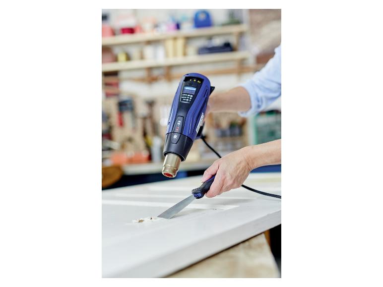 Person verwendet LIVARNO® Heißluftgebläse R2200-LCD zum Abkratzen von Farbe von einer weißen Oberfläche.