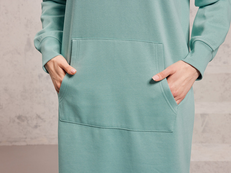 Eine Frau trägt einen hellgrünen Hoodie mit einer großen Tasche.