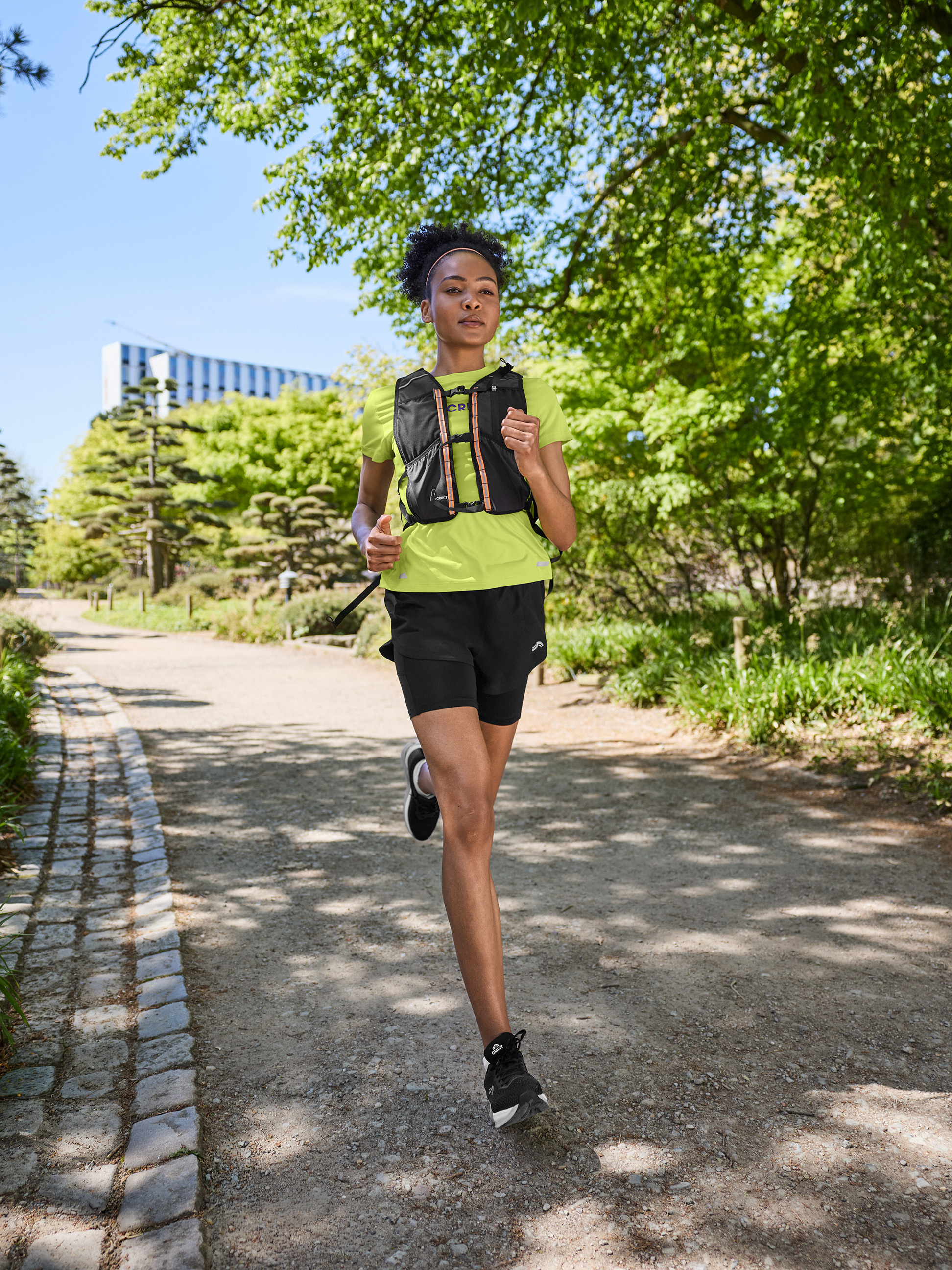 Frau in Sport-T-Shirt, Shorts und Laufweste, joggt auf einem Feldweg.