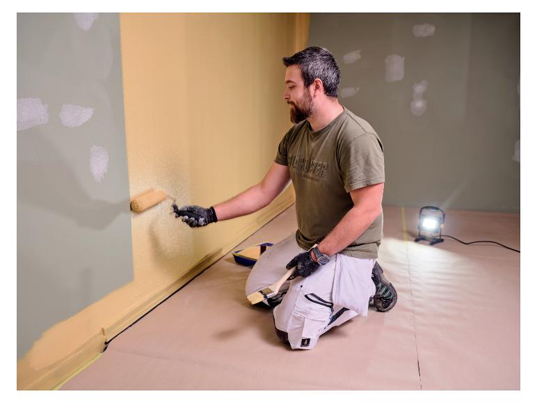 Mann streicht Wand, beleuchtet von LIVARNO® Arbeitslicht »The Painter«.