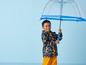 Ein Junge trägt eine Regenjacke mit maritimem Muster und hält einen durchsichtigen Regenschirm.