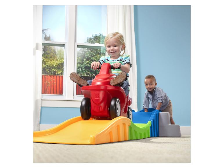 Kinder spielen mit einem roten Spielzeugauto und einer bunten Plastik-Achterbahn.
