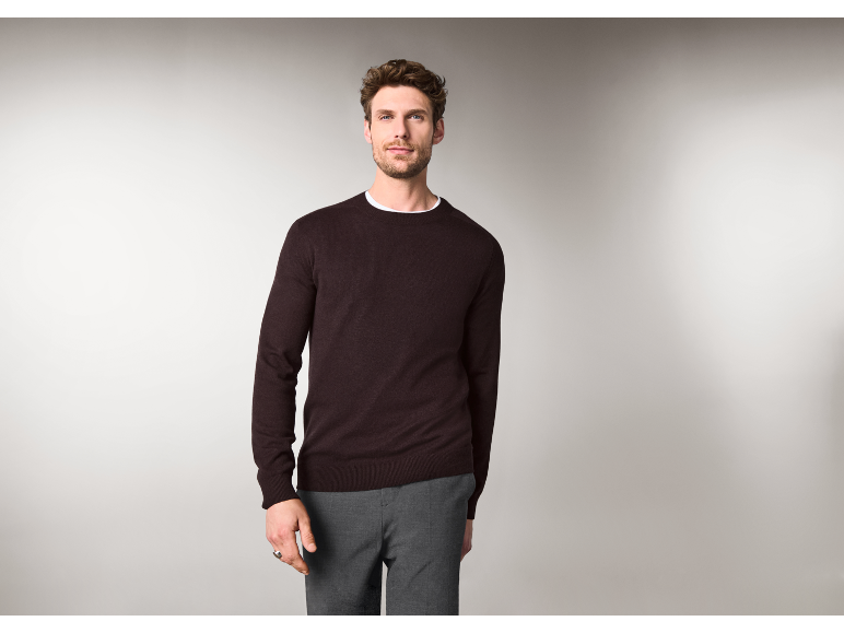 Ein Mann in einem dunkelbraunen Rundhals-Pullover und einer grauen Hose.