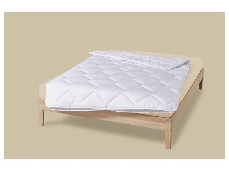 Weiße Bettdecke auf einem Bett mit Holzrahmen.