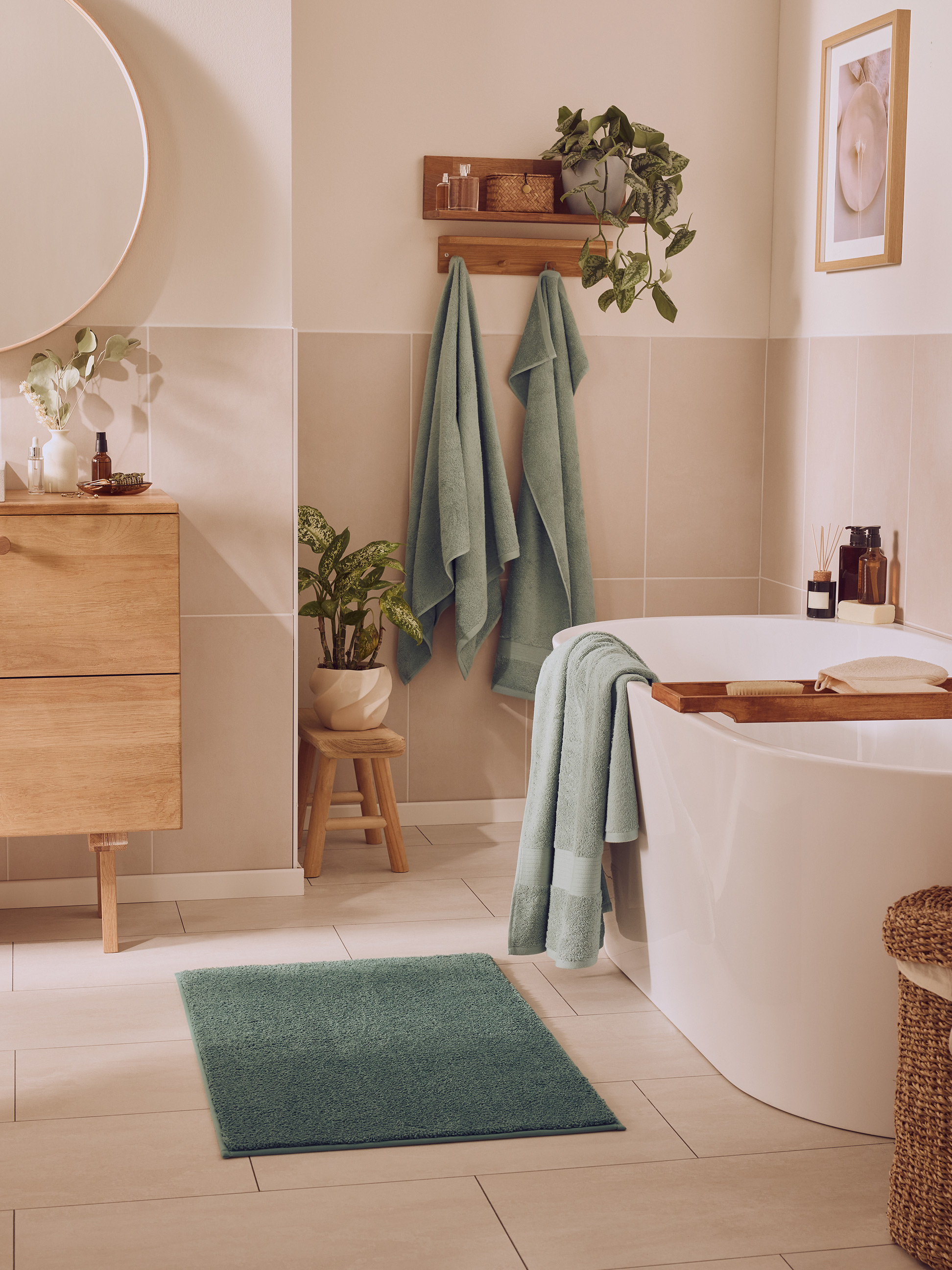 Modernes Badezimmer mit weißer Badewanne, grünen Handtüchern, Holzmöbeln und Pflanzen.