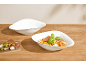 Rigatoni-Nudeln in einer weißen Schale, mit einer leeren Schale und einer Vorspeisenplatte.