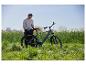 Mann mit einem grauen E-Bike und einer schwarzen Gepäckträgertasche in einem Feld mit gelben Blumen.