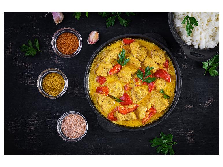 Hähnchen-Curry mit roter Paprika, Reis und Gewürzen auf einem dunklen Holztisch.