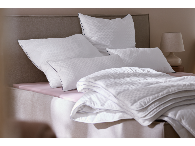 Weiße Bettwäsche und Kissen mit Muster auf einem Bett mit rosa Laken.