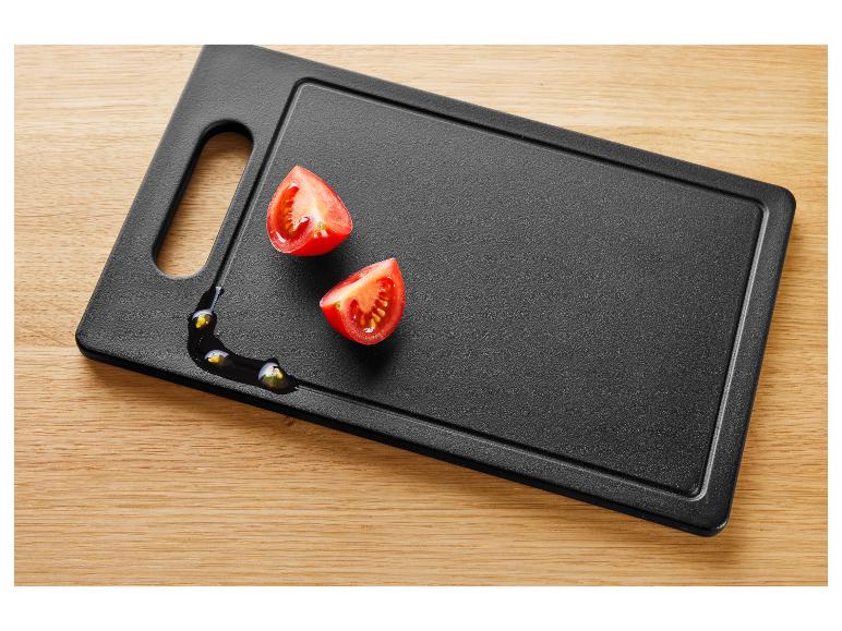 Zwei halbe Kirschtomaten auf einem schwarzen Schneidebrett mit Öl