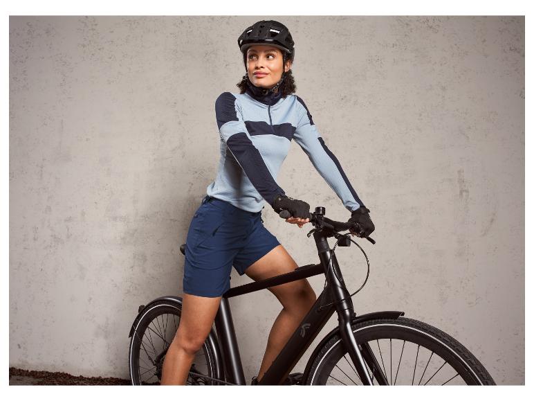 Eine Frau auf einem schwarzen Fahrrad in blauen Radshorts und blau-grauer Sportkleidung.
