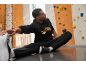 Mann in schwarzem Hoodie und Jogginghose dehnt sich auf dem Boden vor einer Kletterwand.