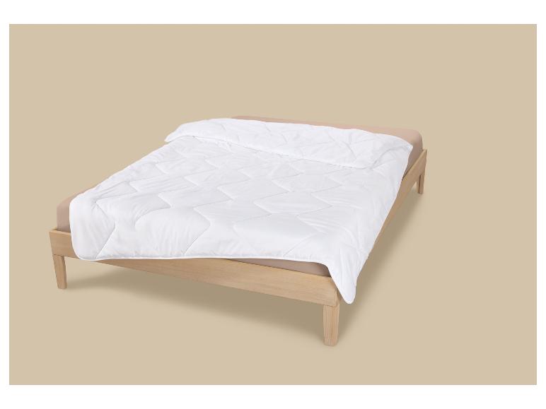 Holzbett mit beiger Bettwäsche und weißer Steppdecke.