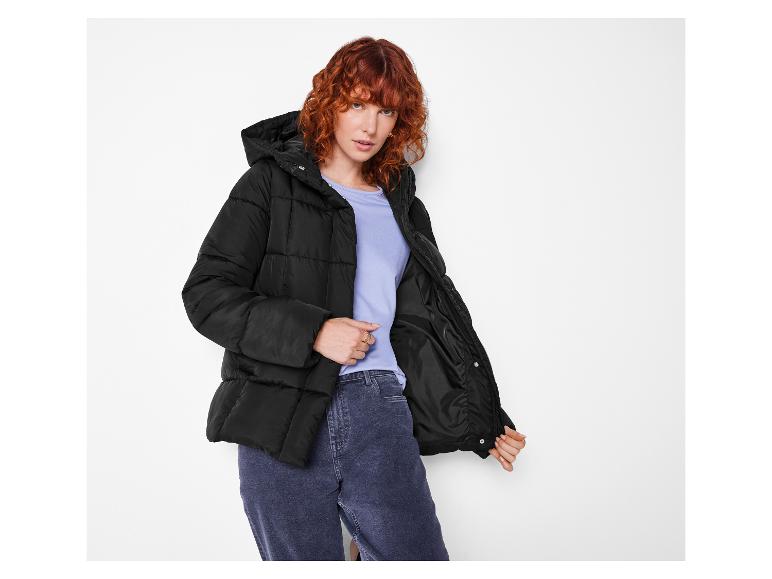 Rothaarige Frau in schwarzer Steppjacke und Jeans.