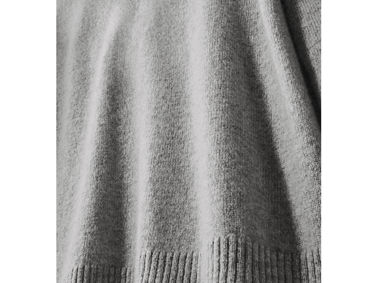Detail eines weichen grauen Strickpullovers mit Rippbündchen.