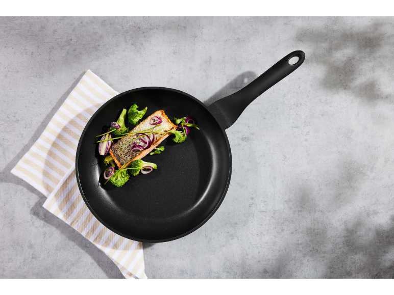 Schwarze Pfanne mit Lachs und Brokkoli auf gestreifter Tischdecke.
