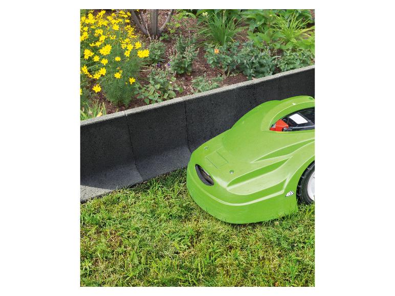 Grüner Mähroboter neben einer dunkelgrauen Gartenbegrenzung und einem Blumenbeet.