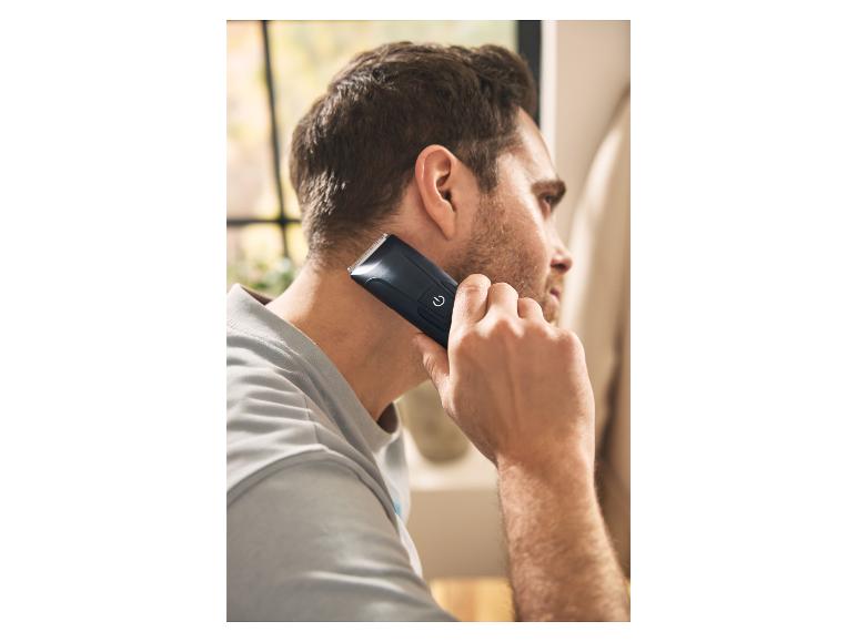 Mann benutzt einen schwarzen Haarschneider, um seinen Nacken zu rasieren.