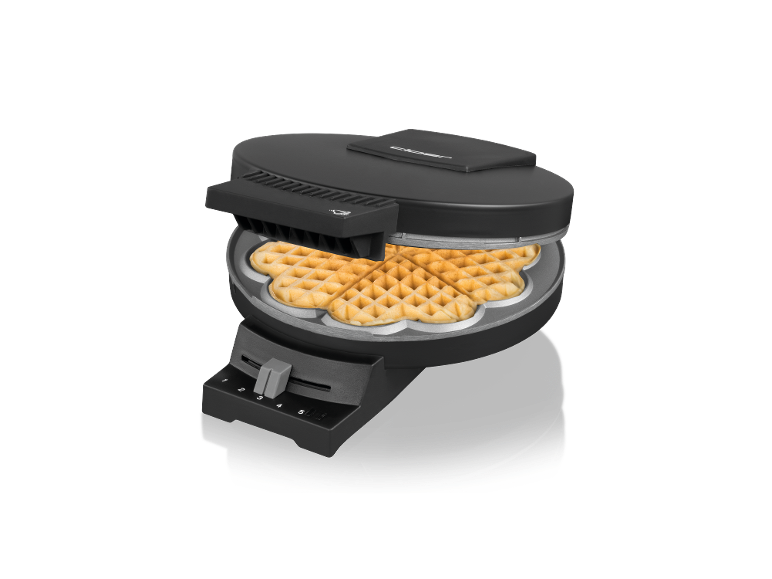 Schwarzes Waffeleisen offen mit einer herzförmigen Waffel darin, auf schwarzem Hintergrund.
