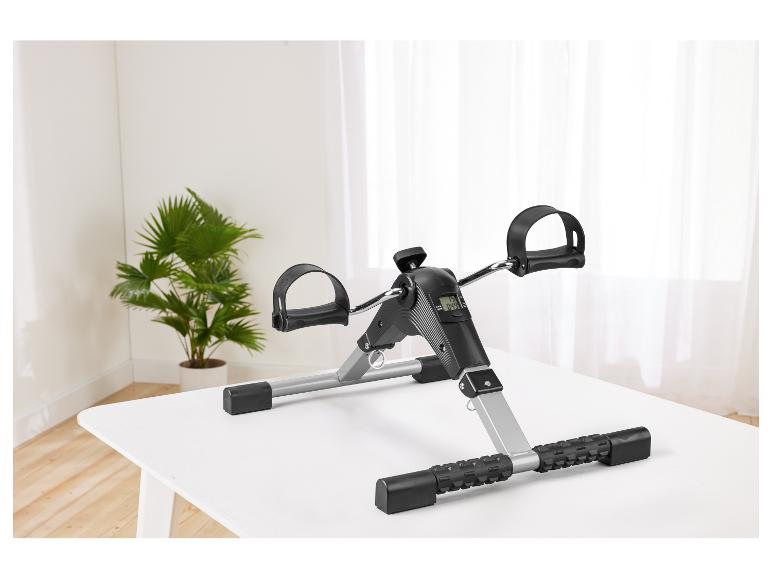 Mini-Heimtrainer mit Digitalanzeige auf einem weißen Tisch, mit Pflanze im Hintergrund.