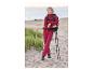 Frau in roter Trekkingjacke und -hose mit Rucksack und Stöcken am Strand.
