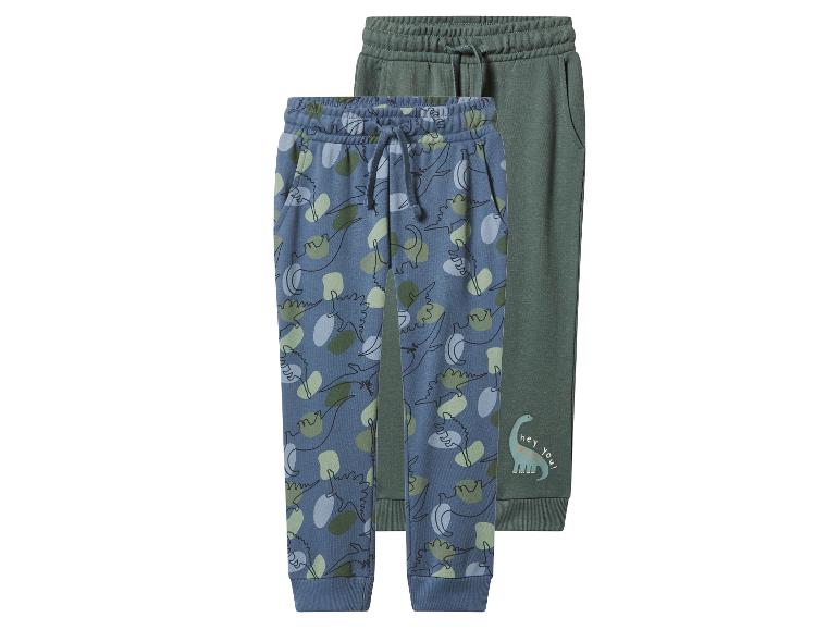 Zwei Kinder-Jogginghosen: eine blaue mit Dinosaurier-Muster und eine grüne mit einem Dinosaurier und dem Text „hey you!“.