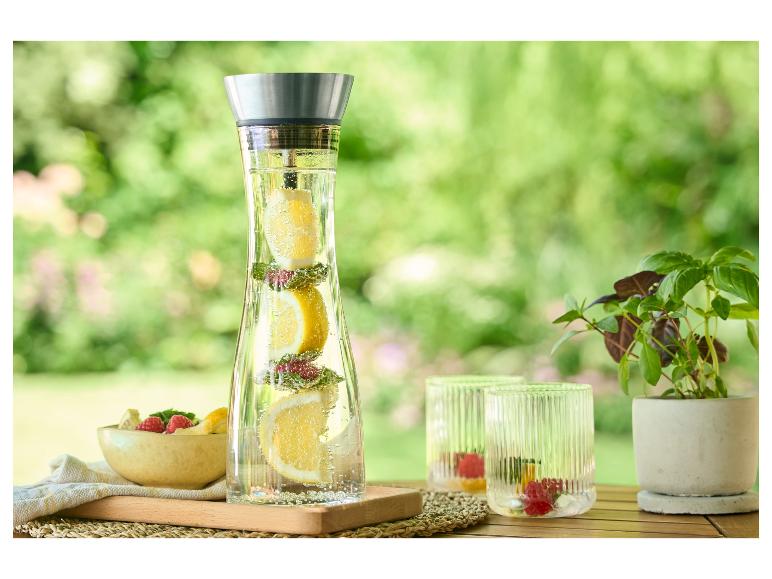 Wasserkaraffe, Gläser und frisches Obst auf einem Tisch im Freien.