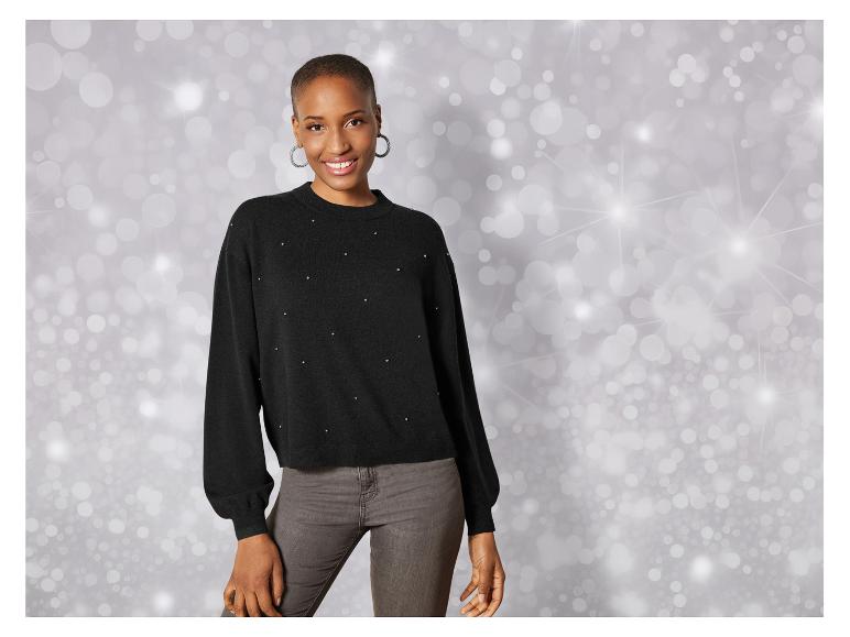 Eine Frau in einem schwarzen Pullover mit Strasssteinen und grauer Jeans.