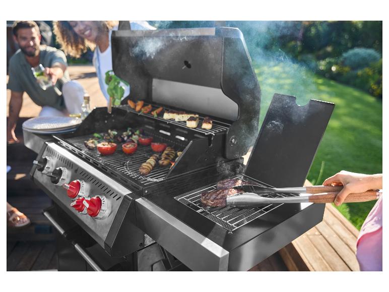 Freunde grillen Fleisch und Gemüse auf einem Gasgrill im Freien.