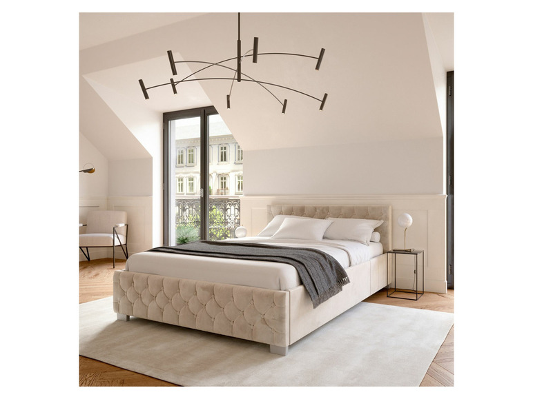 Ein beigefarbenes, gepolstertes Bett mit einem modernen Kronleuchter in einem Schlafzimmer.