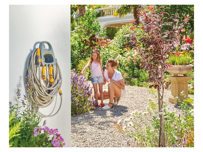 Gartenschlauchhalter mit Zubehör an weißer Wand, mit Frau und Kind im Garten.