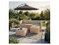Outdoor-Rattan-Sofagarnitur mit beigen Kissen, Glastisch und großem Sonnenschirm auf einer Terrasse.