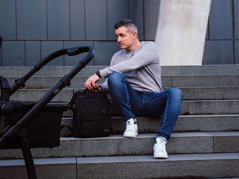Ein Mann sitzt auf den Stufen mit einem Ole Kinderwagen und einer Samsonite-Rucksack.