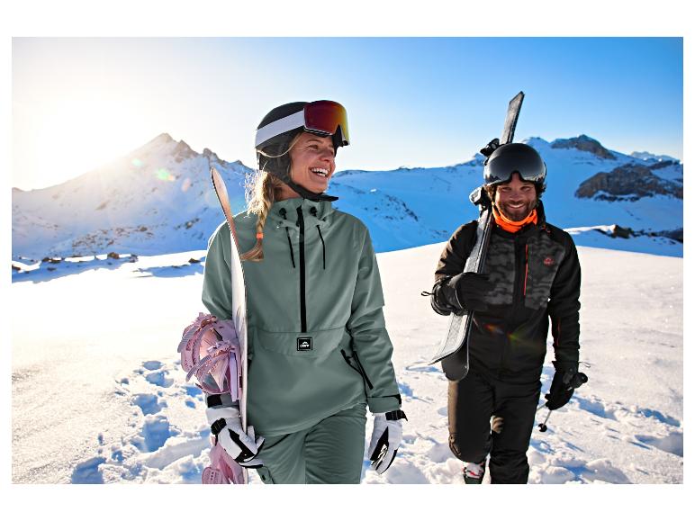 Frau in graugrüner Crivit Skijacke mit Snowboard neben einem Mann im Schnee.