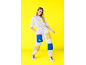 Frau in weißem T-Shirt und weißer Cargohose mit blauen und gelben Taschen.