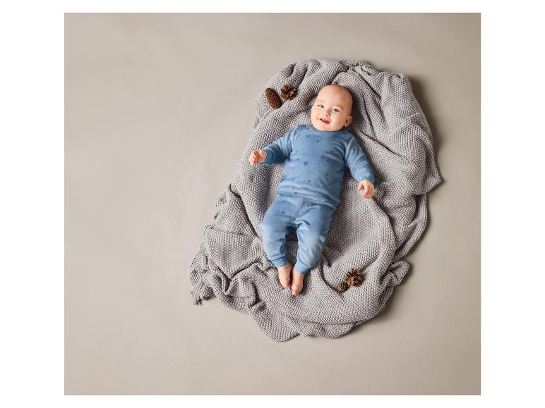 Ein Baby liegt auf einer grauen Decke in einem blauen Sternchen-Strampler.