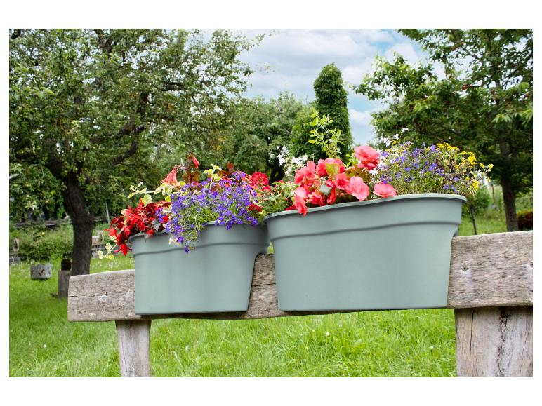 Blumenkästen mit bunten Blumen, die an einem Holzzaun in einem grünen Garten hängen.