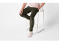 Mann in hellrosa T-Shirt und dunkelgrüner Cordhose sitzt auf einem weißen Hocker.