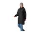 Frau in schwarzer Regenjacke, blauen Jeans und grauer Mütze, lächelnd und gehend.