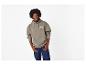 Mann in einem khakifarbenen Hoodie mit dem Text „23 OUT OF THIS WORLD“ und dunkelblauen Jeans