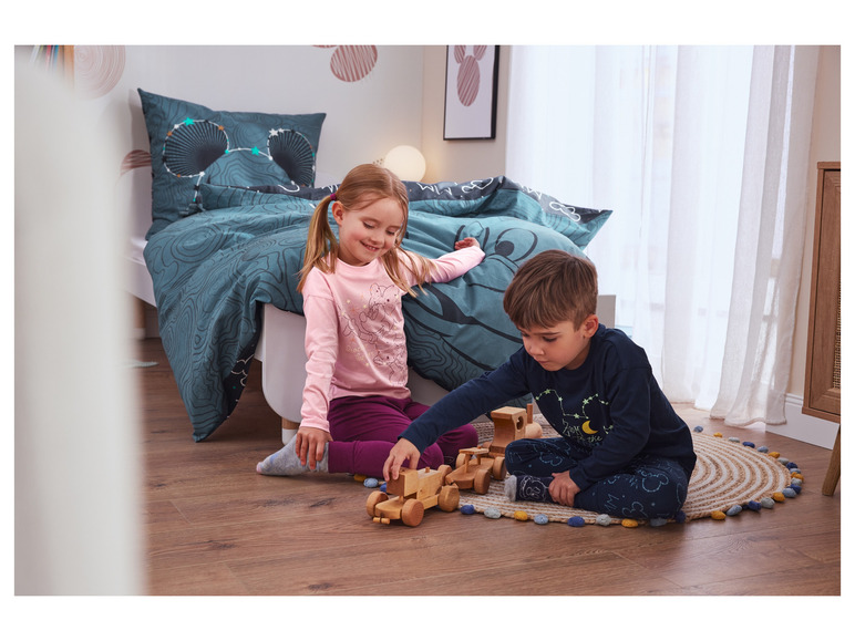 Zwei Kinder spielen mit Holzspielzeug auf einem Teppich.